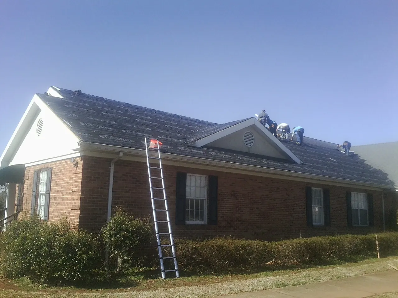 Crew tearing shingles off a brick ranch roof with a ladder set — Metal Roof Repair work by our crew in Bishop