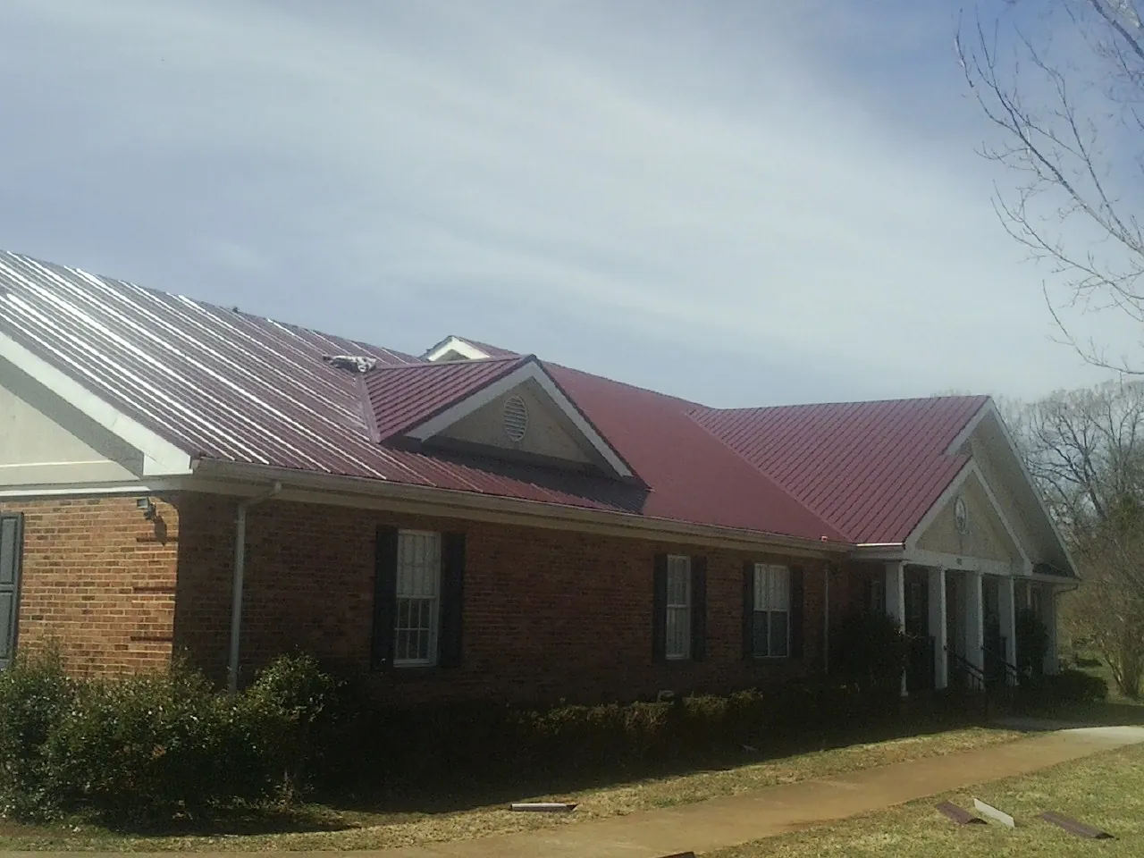 Red metal roof with gabled entries on a long brick building, from a Hail Damage Roof Repair job in Bishop