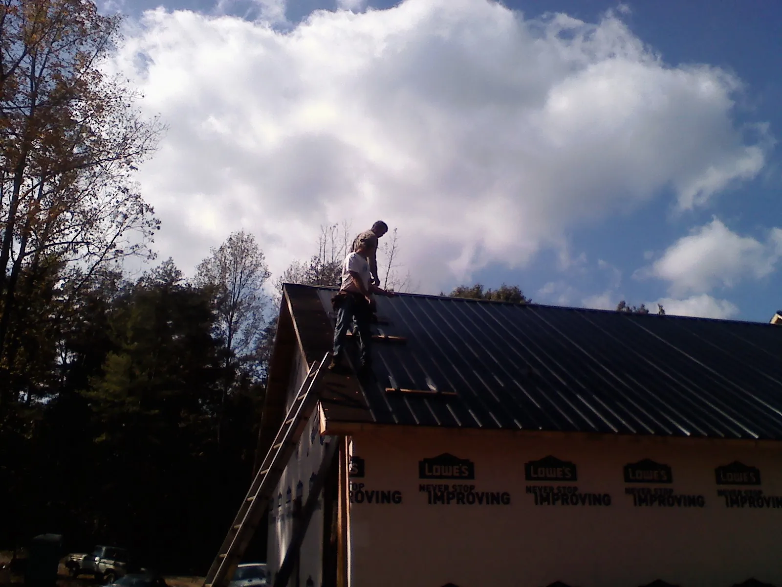 Roofer fastening dark metal panels high against a cloudy sky, from a Roof Inspection job in Bishop